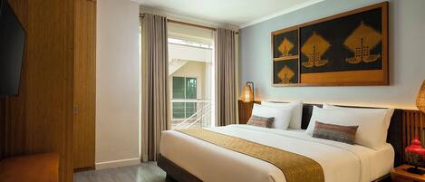 A hotel room with a large bed, a wooden wardrobe, a desk, and a window with curtains.