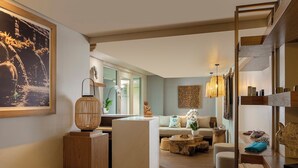 A modern living room with a sofa, coffee table, and decorative items. There is a wooden bookshelf and a large window providing natural light. - Anantara Vacation Club Legian (Legian)
