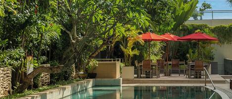 A pool area with a curved edge, surrounded by lush greenery and red umbrellas.