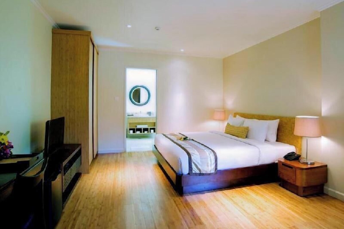 A hotel room with a bed, bedside table, lamp, and a view of a bathroom with a mirror.