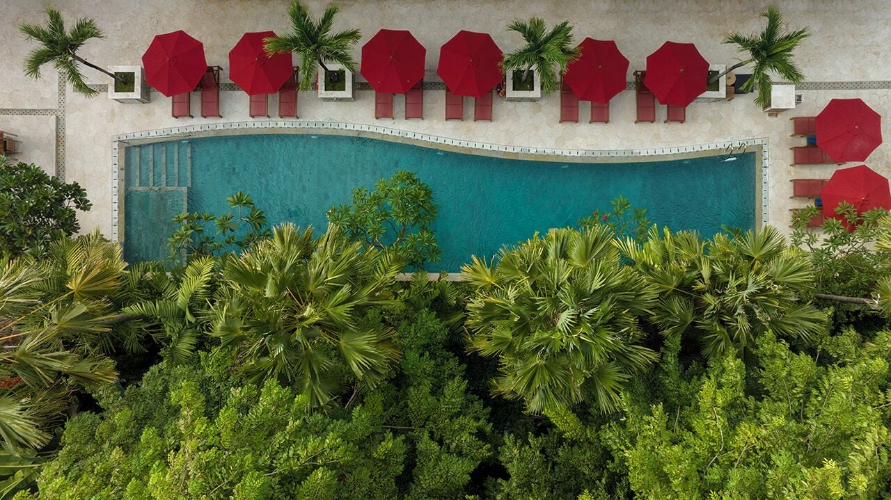 Une piscine bordée de parasols rouges et de palmiers.