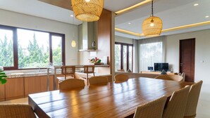 A spacious dining area with a long wooden table, wicker chairs, and hanging wicker lamps. - Breeze Blows City View 5 Br Heated Pool and a Billiard (Cimenyan)