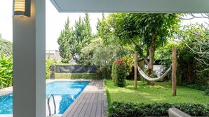 A swimming pool with a wooden deck, surrounded by greenery and a hammock. - Breeze Blows City View 5 Br Heated Pool and a Billiard (Cimenyan)