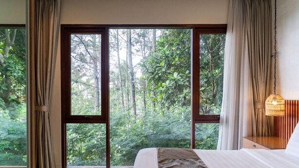 A bedroom with a large window, a bed, a bedside table, and a hanging light fixture. - Breeze Blows City View 5 Br Heated Pool and a Billiard (Cimenyan)