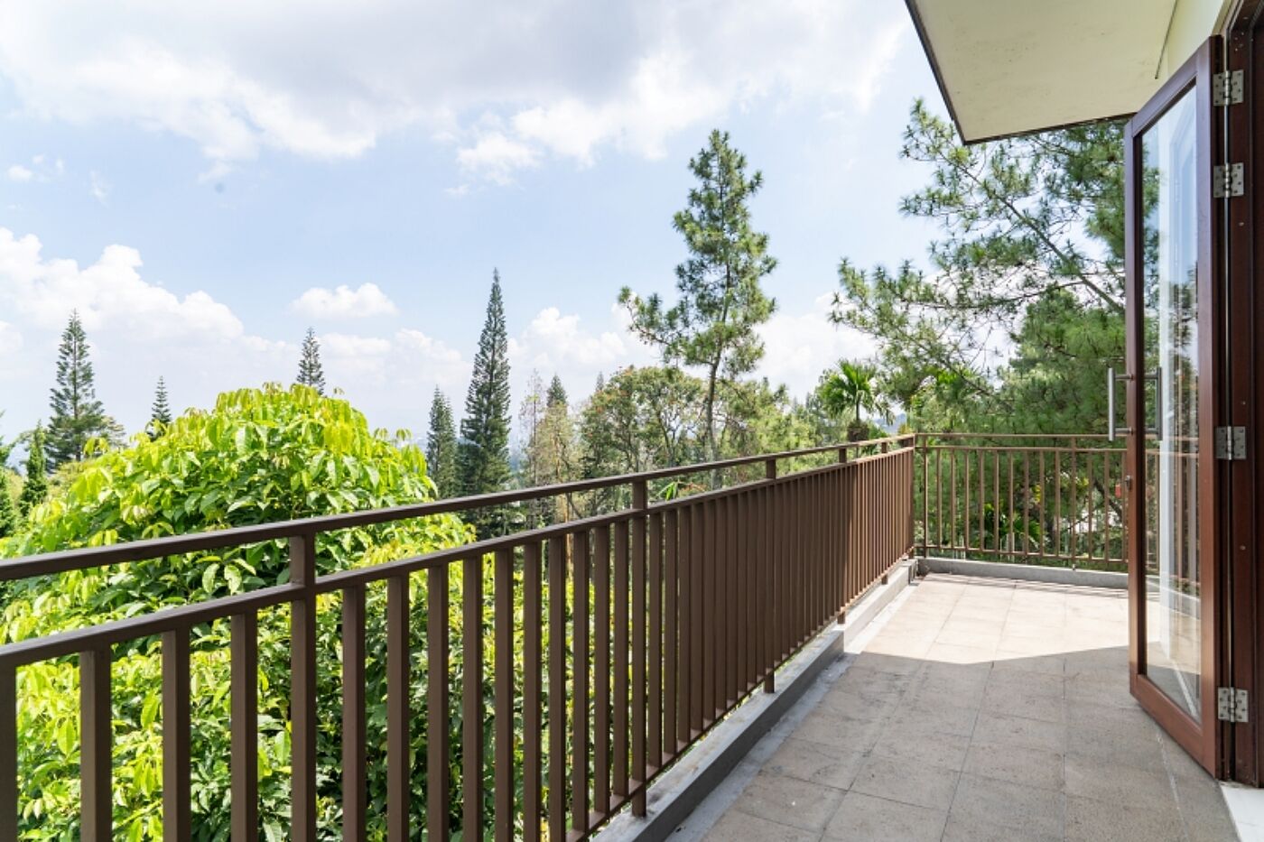 A balcony with a metal railing, a glass door, and a view of trees and sky.