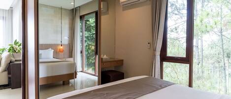 A modern bedroom with a large bed, a mirror, an air conditioning unit, and a view of trees through the window.
