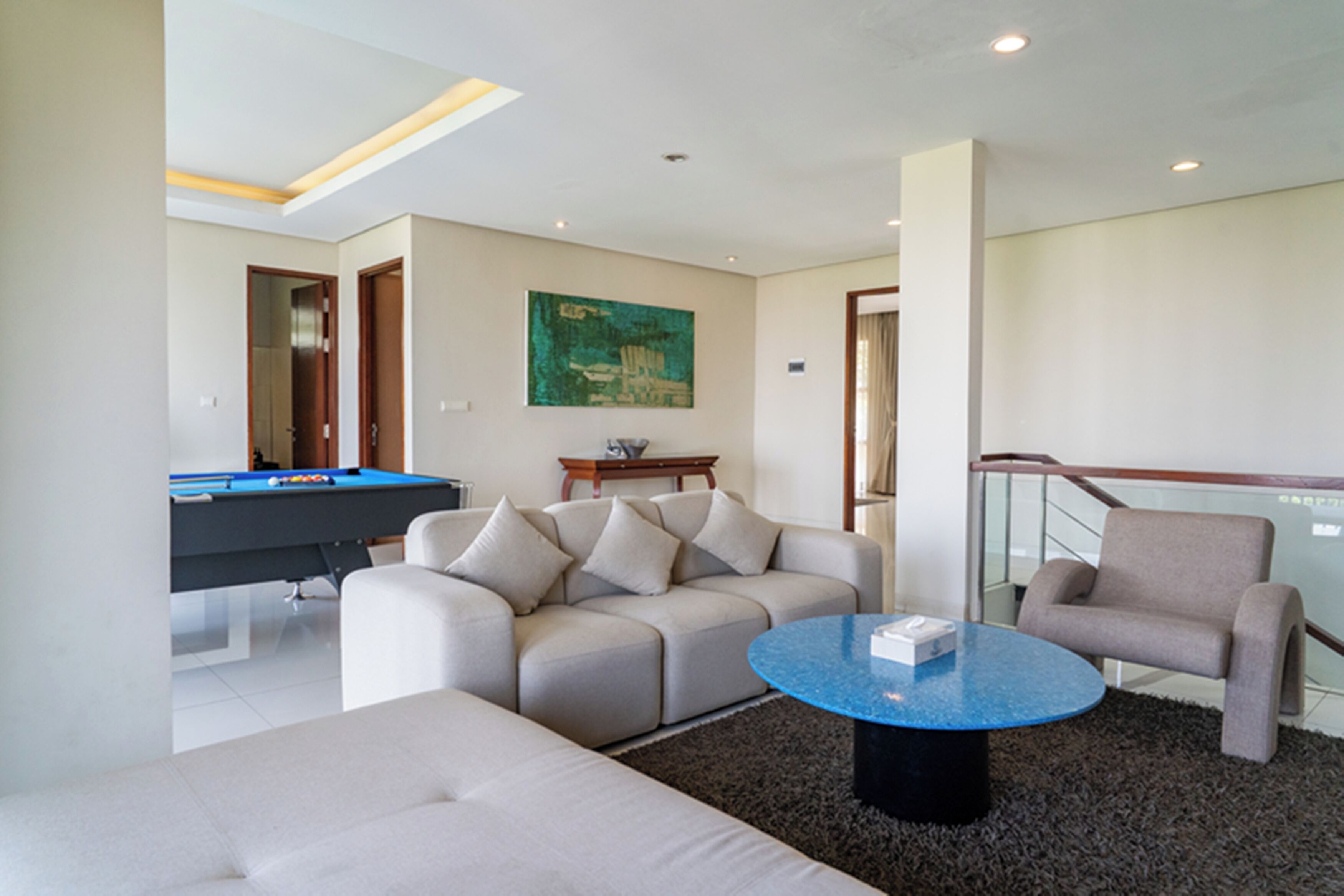 A modern living room with a pool table, a sofa, a coffee table, and a painting on the wall.