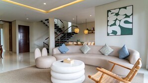 A modern living room with a sofa, a round coffee table, a wicker chair, and a staircase in the background. - Breeze Blows City View 5 Br Heated Pool and a Billiard (Cimenyan)