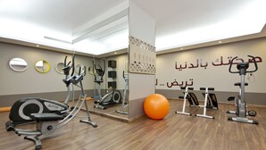 Une salle de sport équipée de divers appareils d’exercice, notamment des vélos elliptiques et un vélo d’appartement, ainsi qu’un grand ballon d’exercice orange.