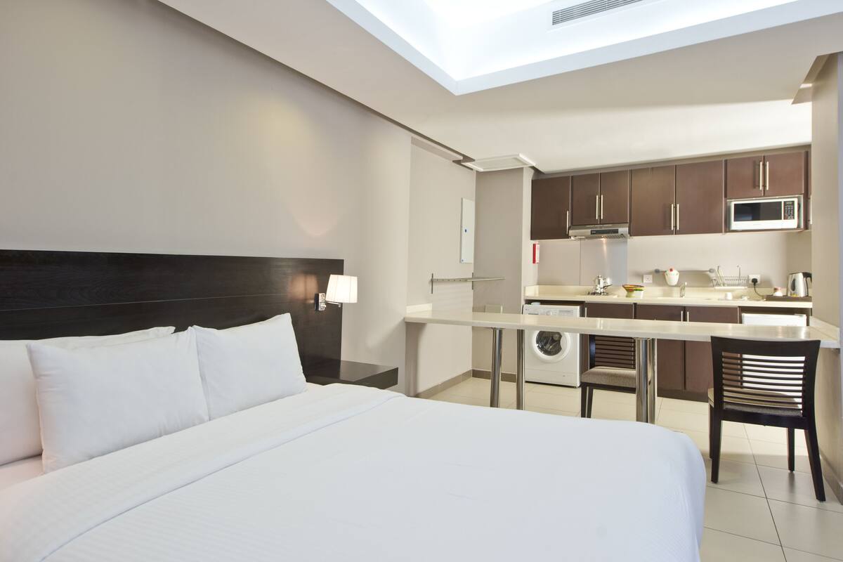 A hotel room with a large bed, a small kitchenette, and a view of the sky through the ceiling.