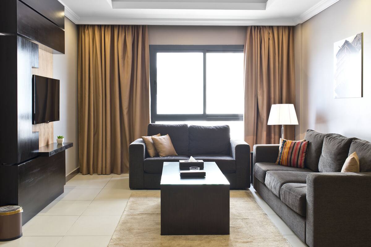 A modern living room with a dark sofa, a coffee table, a TV, and a window with curtains.