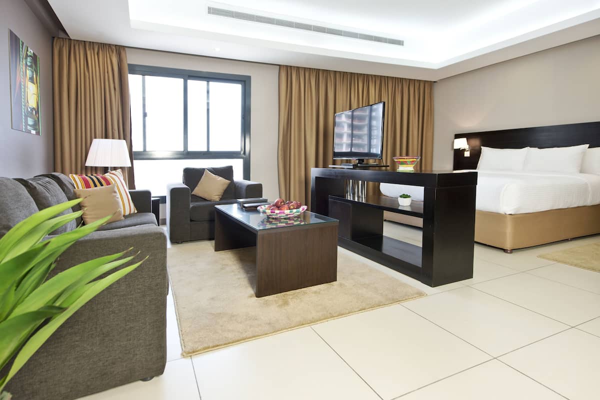 A modern hotel room with a sofa, a coffee table, a TV, a bed, and a large window.