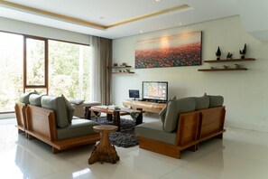 A modern living room with two sofas, a coffee table, and a TV. There is a large window and a painting on the wall. - Ohara City View 5BR Villa Heated Pool and Billiard (Bandung)