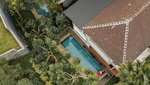 Vue aérienne d’une propriété résidentielle dotée d’une piscine, entourée d’une végétation luxuriante et comprenant une maison avec un toit en pente.