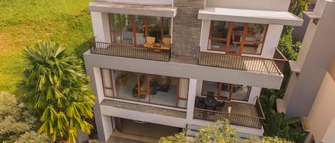 A multi-story residential building with balconies, large windows, and a car parked in the driveway.