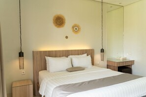 Een slaapkamer met een houten hoofdeinde, een bed met witte beddengoed, twee wandlampen en een spiegel boven een houten wastafelmeubel.