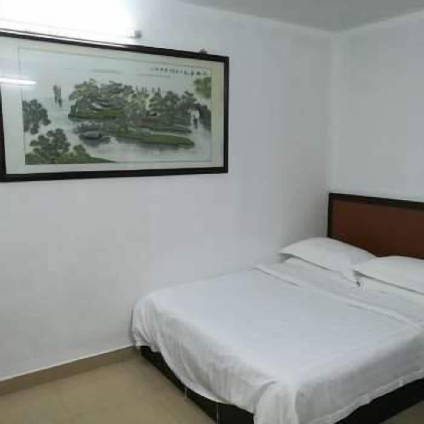 A simple room with a bed, a framed picture on the wall, and a plain white ceiling.