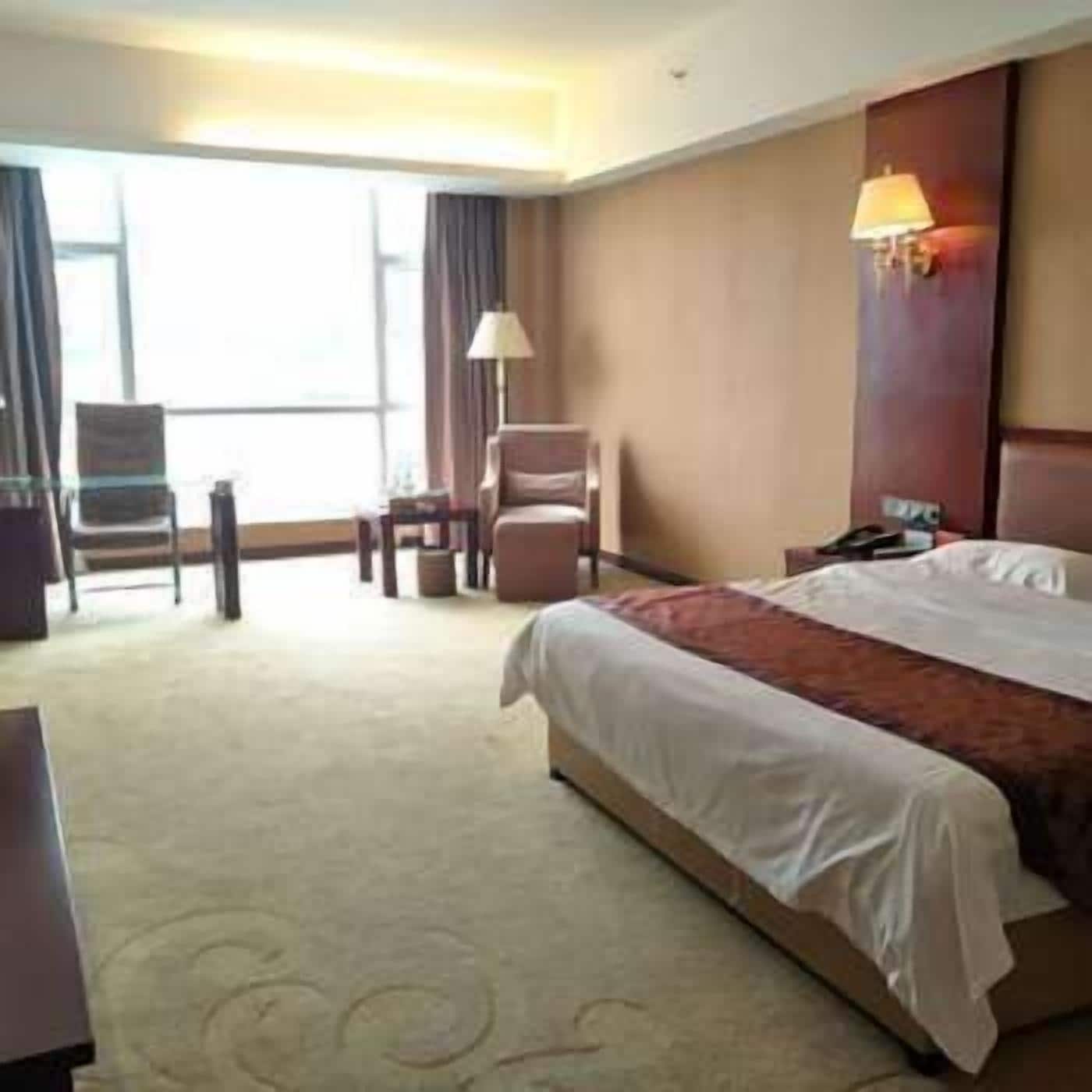 A hotel room with a large bed, a desk, a chair, and a lamp.