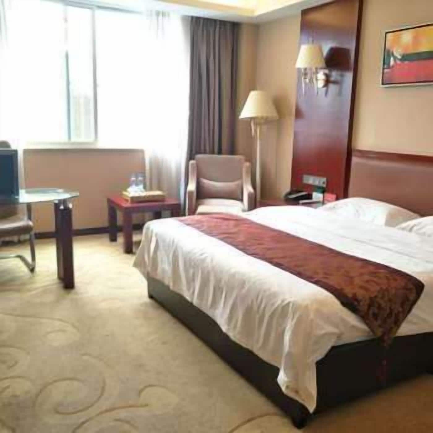 Une chambre d’hôtel avec un grand lit, un bureau, une chaise, une lampe et un tableau au mur.