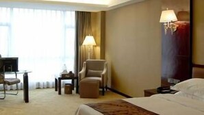 Habitación de hotel con cama, escritorio, silla, lámpara y ventana con cortinas.
