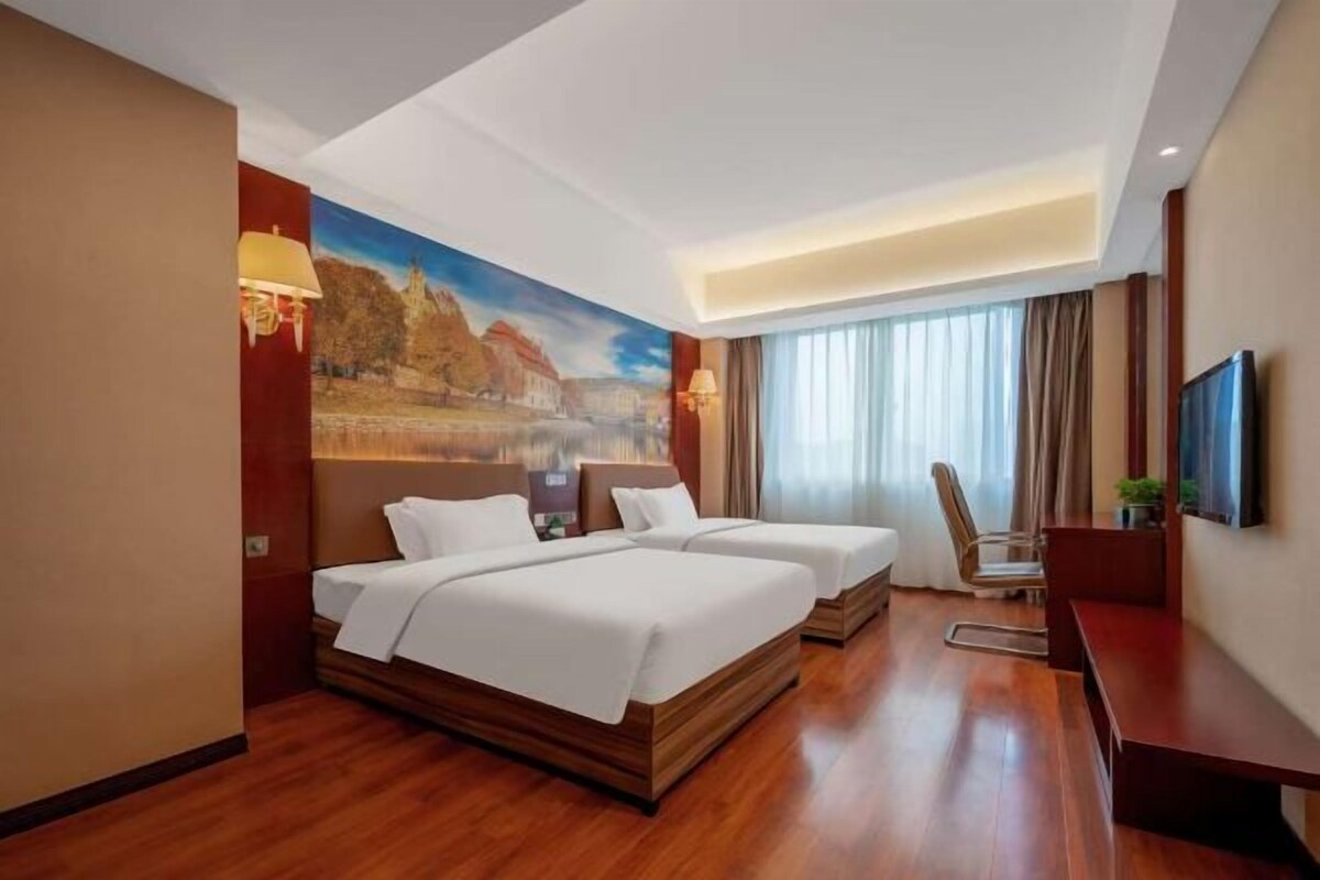 A hotel room with two beds, a desk, a chair, and a TV.