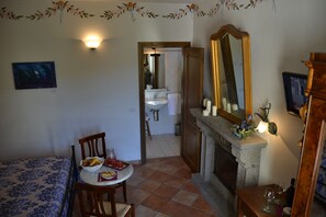 Un dormitori amb llit, taula de dinar amb esmorzar, una llar de foc i un bany visible a través d'una porta oberta.