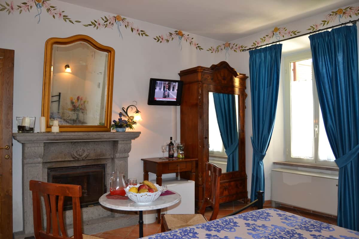 A room with a fireplace, a mirror, a television, a table with fruit, and a bed with a floral bedspread.