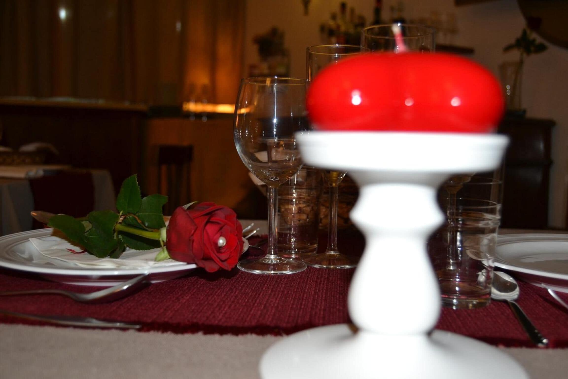 A dining table with a red rose, wine glasses, and a white plate.
