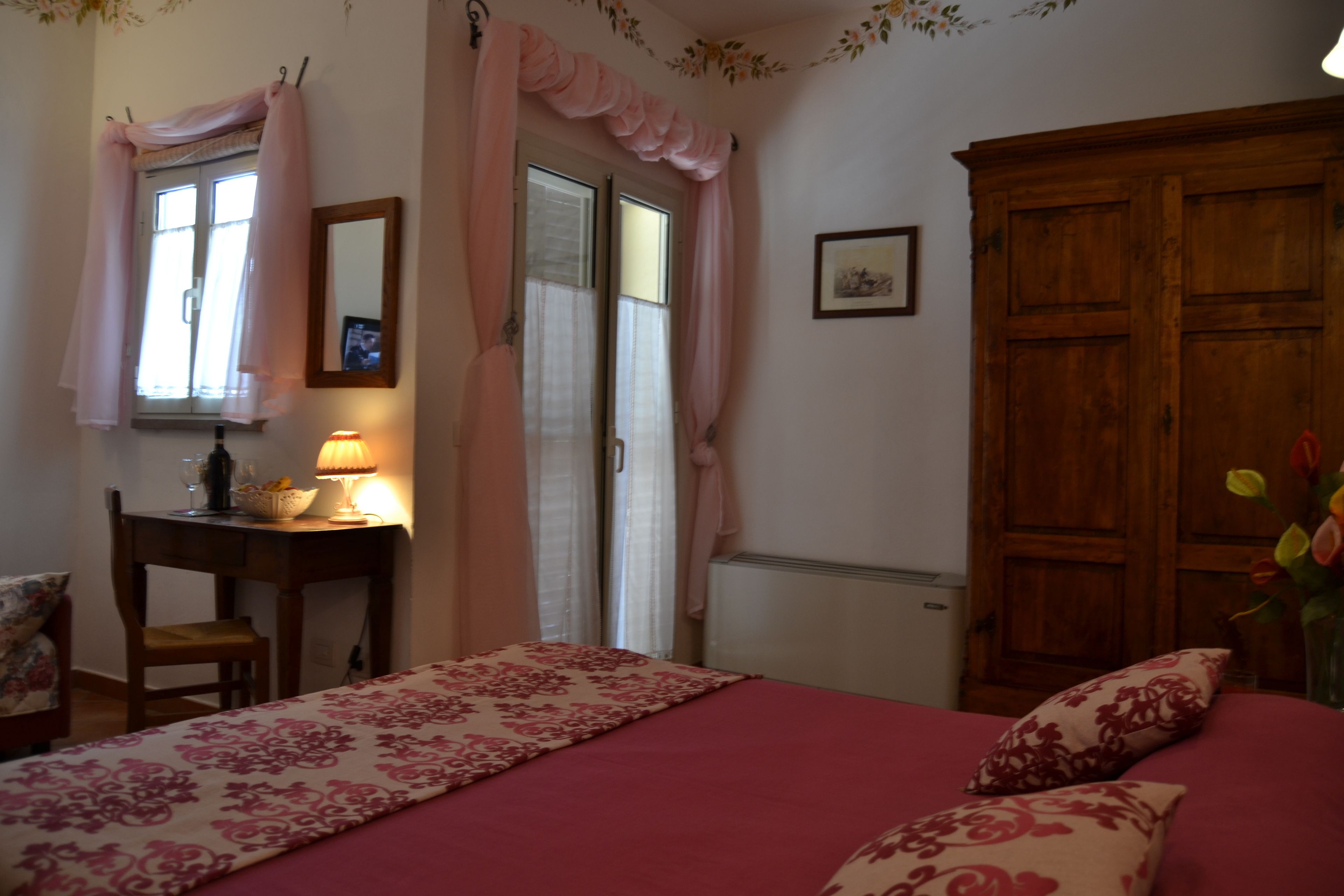 Un dormitorio con una cama, un escritorio con lámpara, una silla, un armario de madera y una ventana con cortinas.