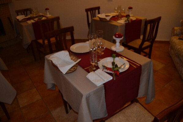 Un espace repas avec des tables dressées pour deux personnes, chacune agrémentée d’une nappe blanche, de serviettes rouges et d’un centre de table composé d’une rose rouge.
