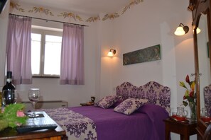 Un dormitori amb un llit, cortines, un quadre, una tauleta de nit, un mirall i una finestra.