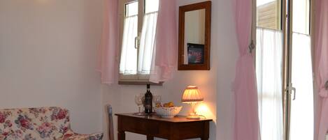 A bedroom with a bed, a chair, a table with a lamp, a mirror, and a window with curtains.