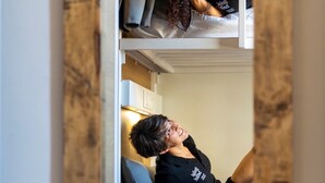 Habitación con literas de madera, una persona sentada en la litera inferior y otra acostada en la superior.