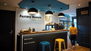 Zona de recepción con un cartel que dice "Factory Hostels Barcelona", una máquina de escribir y un letrero de bienvenida.