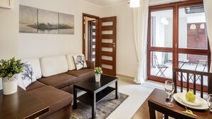 A modern living room with a brown sofa, a black coffee table, and a dining table with a plate of fruit and a wine glass. - Tatrytop Apartamenty Tetmajer (Zakopane)