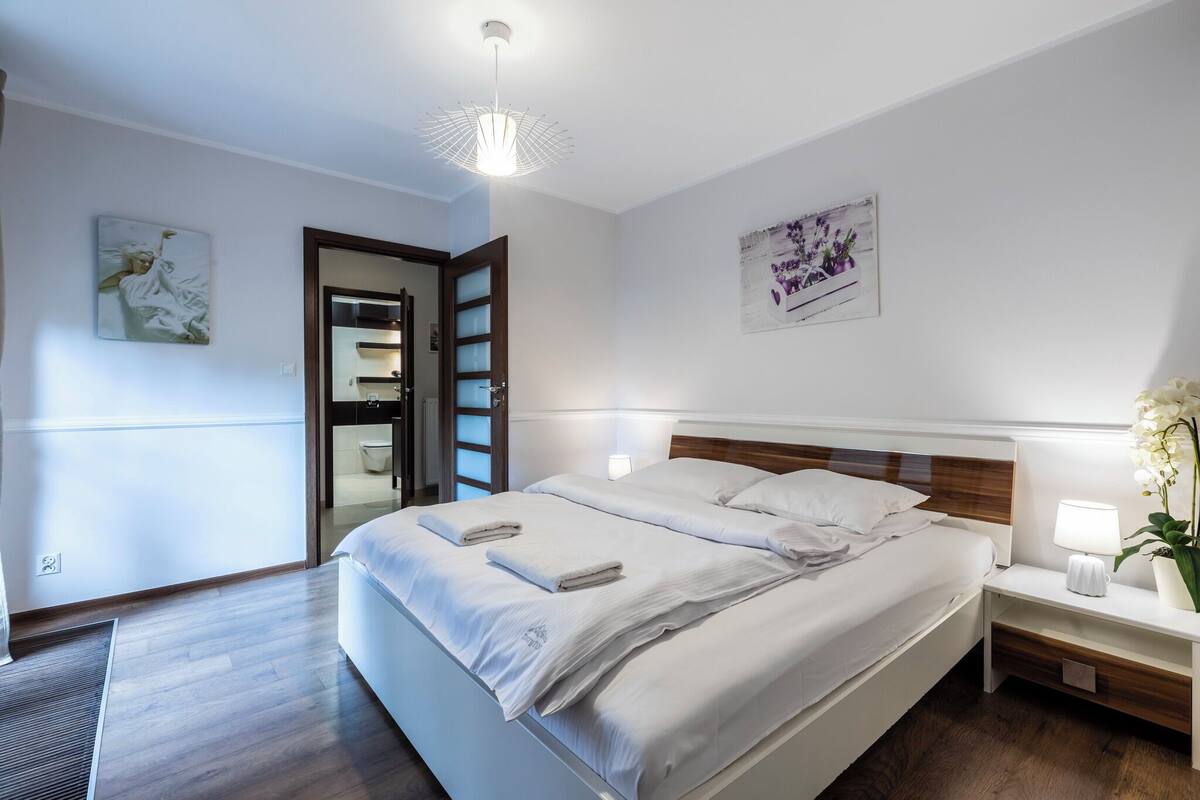 Une chambre d’hôtel moderne, dotée d’un grand lit, de tables de chevet, d’une petite table avec une lampe et d’œuvres d’art accrochées aux murs.