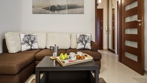A living room with a brown sofa, a coffee table with a tray of food, and a cityscape painting on the wall. - Tatrytop Apartamenty Tetmajer (Zakopane)