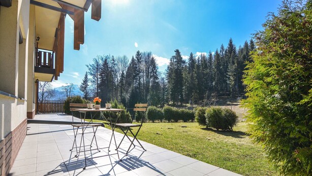 A patio with a table and chairs, a small garden, and a view of a forest and mountains.