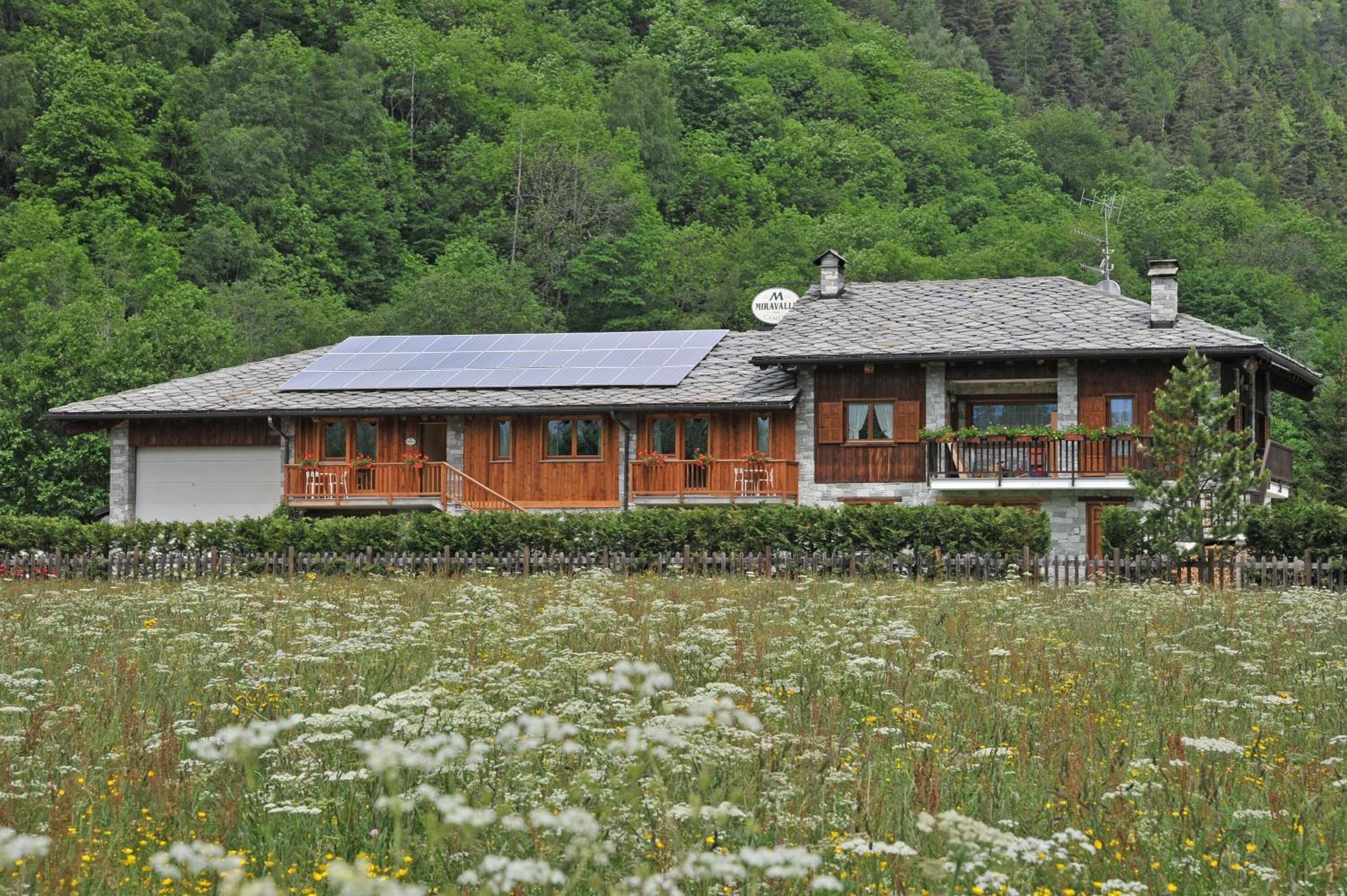 Una casa de madera con balcón, paneles solares y un bosque al fondo.