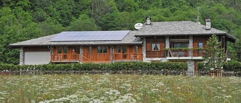 Una casa de madera con balcón, paneles solares y un bosque al fondo.