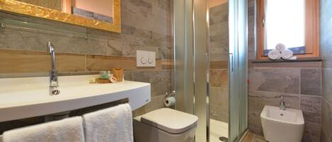 A bathroom with a glass-enclosed shower, a sink, a toilet, and a bidet.