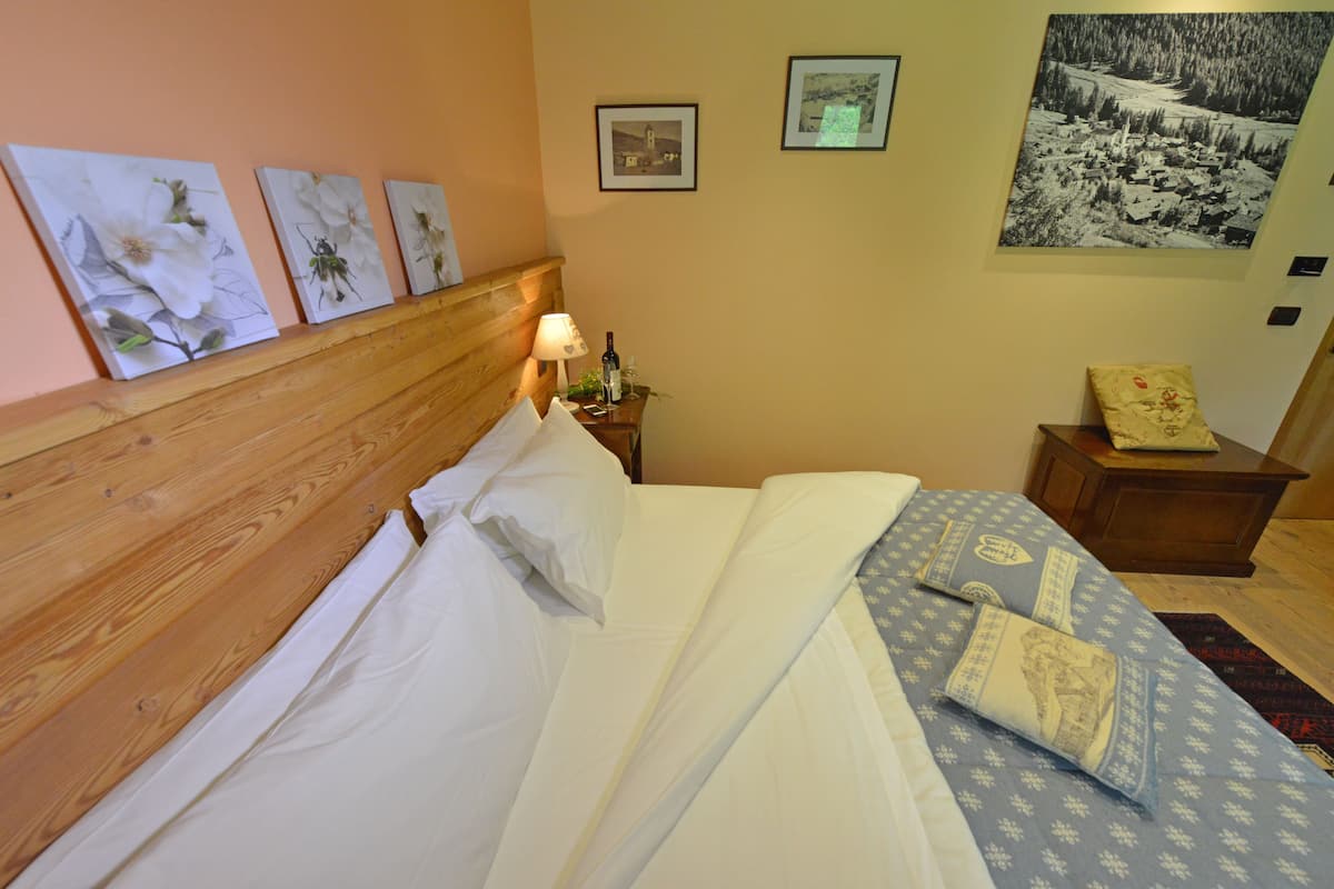 Un lit bien fait, avec du linge de lit blanc, une tête de lit en bois et une table de chevet sur laquelle se trouvent une lampe et une bouteille.