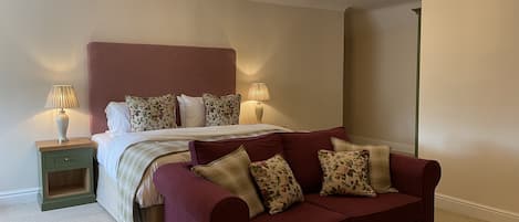 A bedroom with a bed, a red sofa, two bedside tables with lamps, and a chandelier.