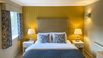 A hotel room with a large bed, two bedside tables, a nightstand, a lamp, a telephone, and a window with curtains.