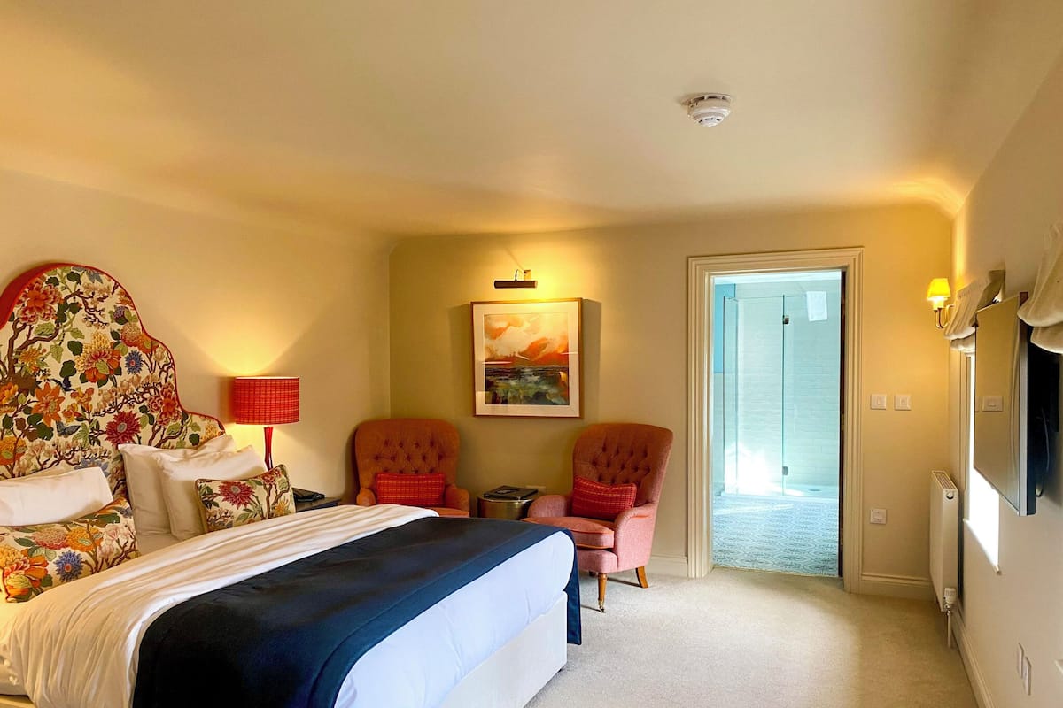 A hotel room with a large bed, two armchairs, a small table, and a painting on the wall.