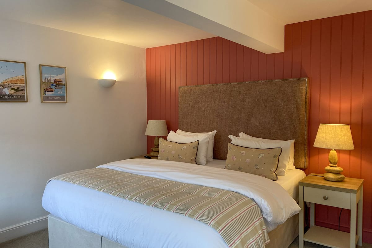 A neatly arranged bedroom with a large bed, two bedside tables with lamps, and two framed pictures on the wall.
