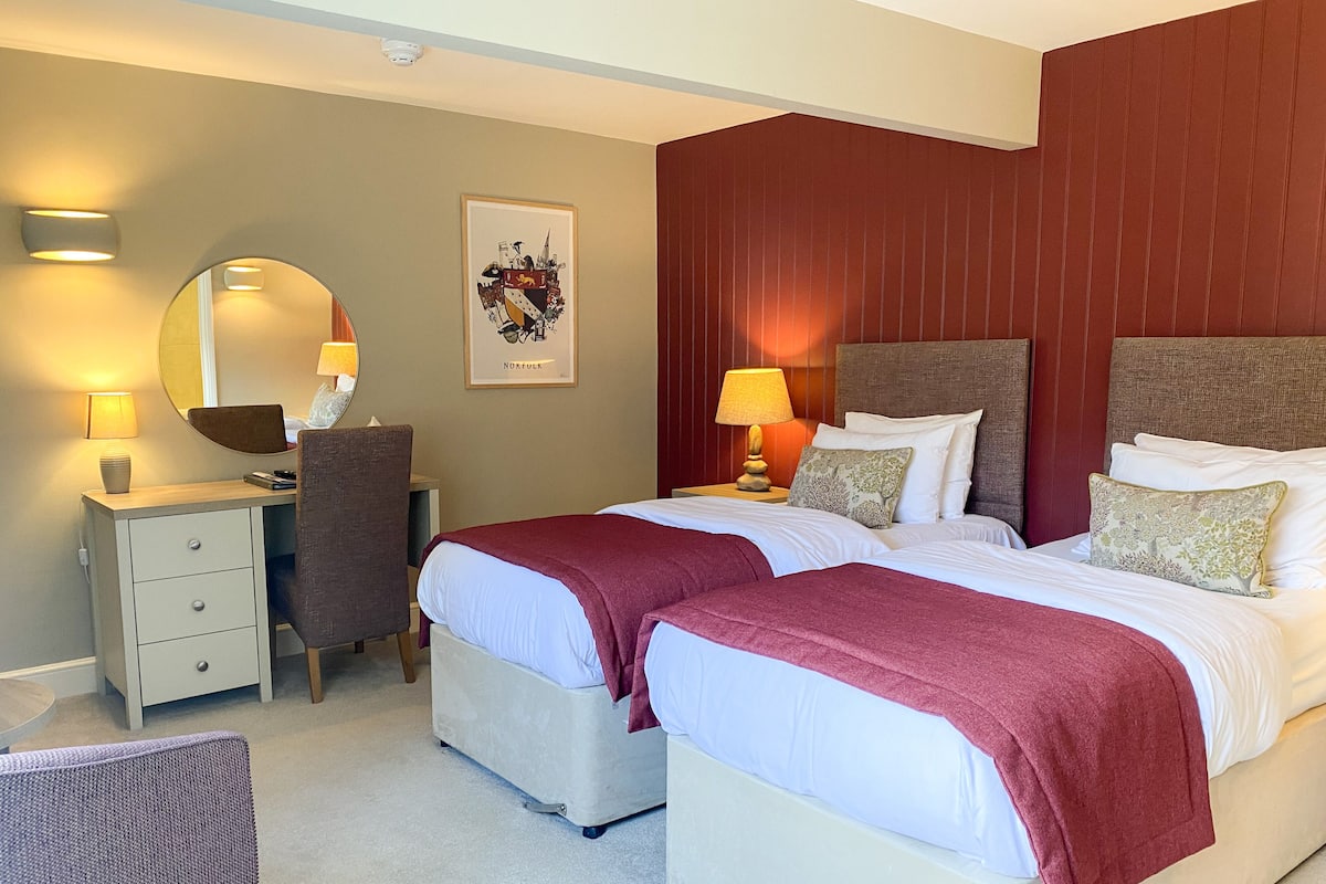 A hotel room with two beds, a desk, a chair, and a mirror.