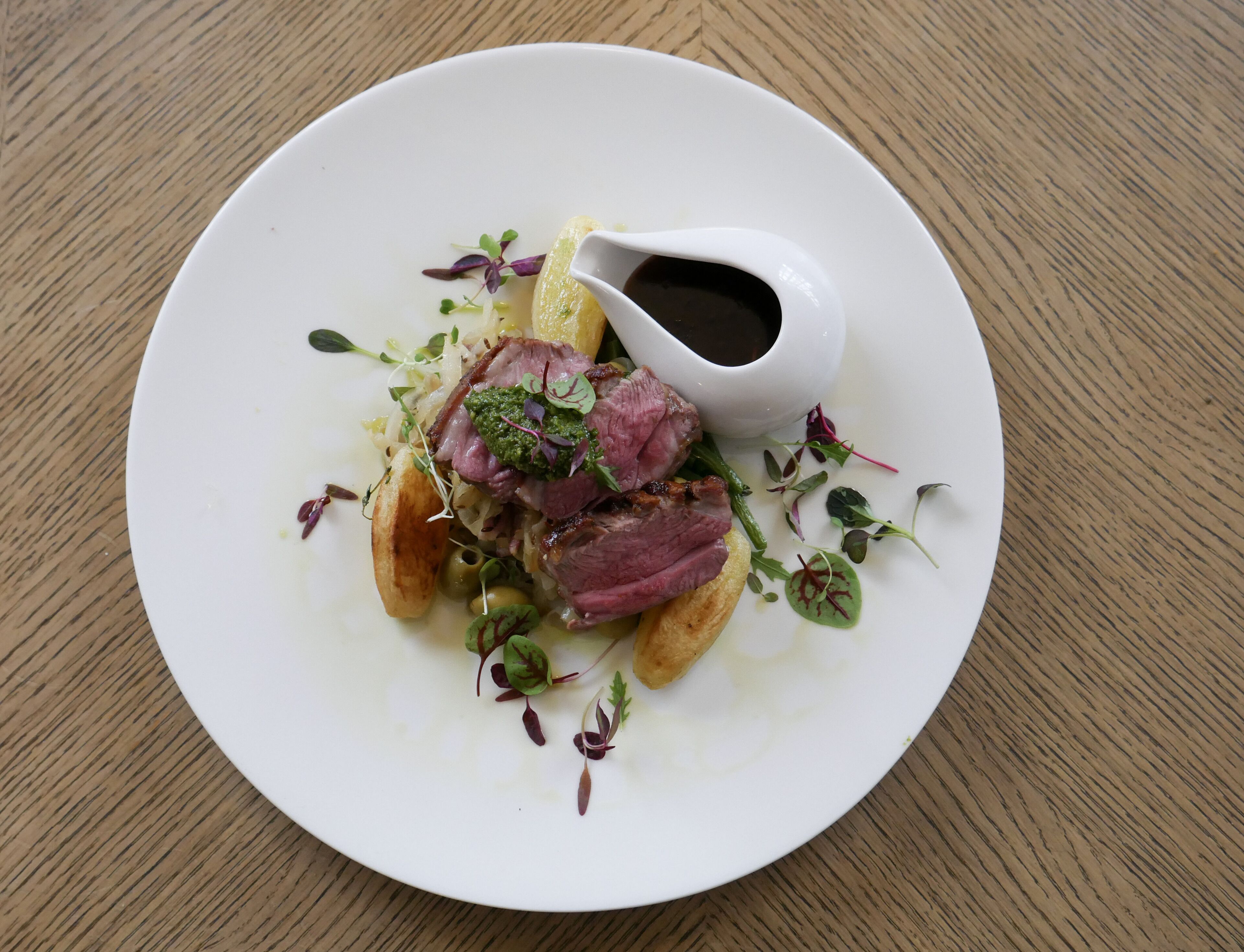 A white plate with a dish of meat, vegetables, and sauce on a wooden table.