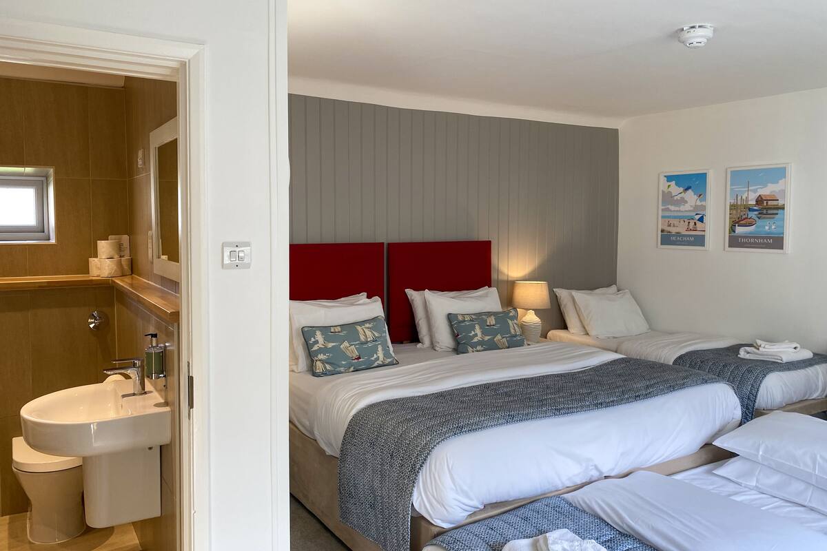 A hotel room with two beds, a red headboard, a sink, and a toilet. There are two framed pictures on the wall.