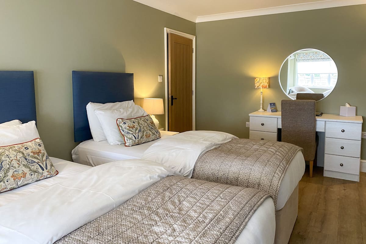 A hotel room with two beds, a desk with a chair, a mirror, and a door.